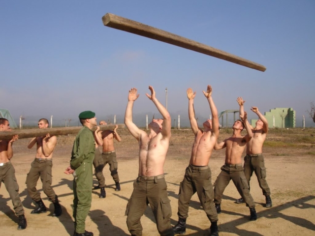 4 men throwing a log into the air, while the Sargent checks how high it goes